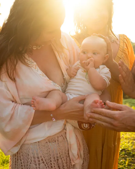 Two women holding a baby between them in low golden light, the sun flaring behind